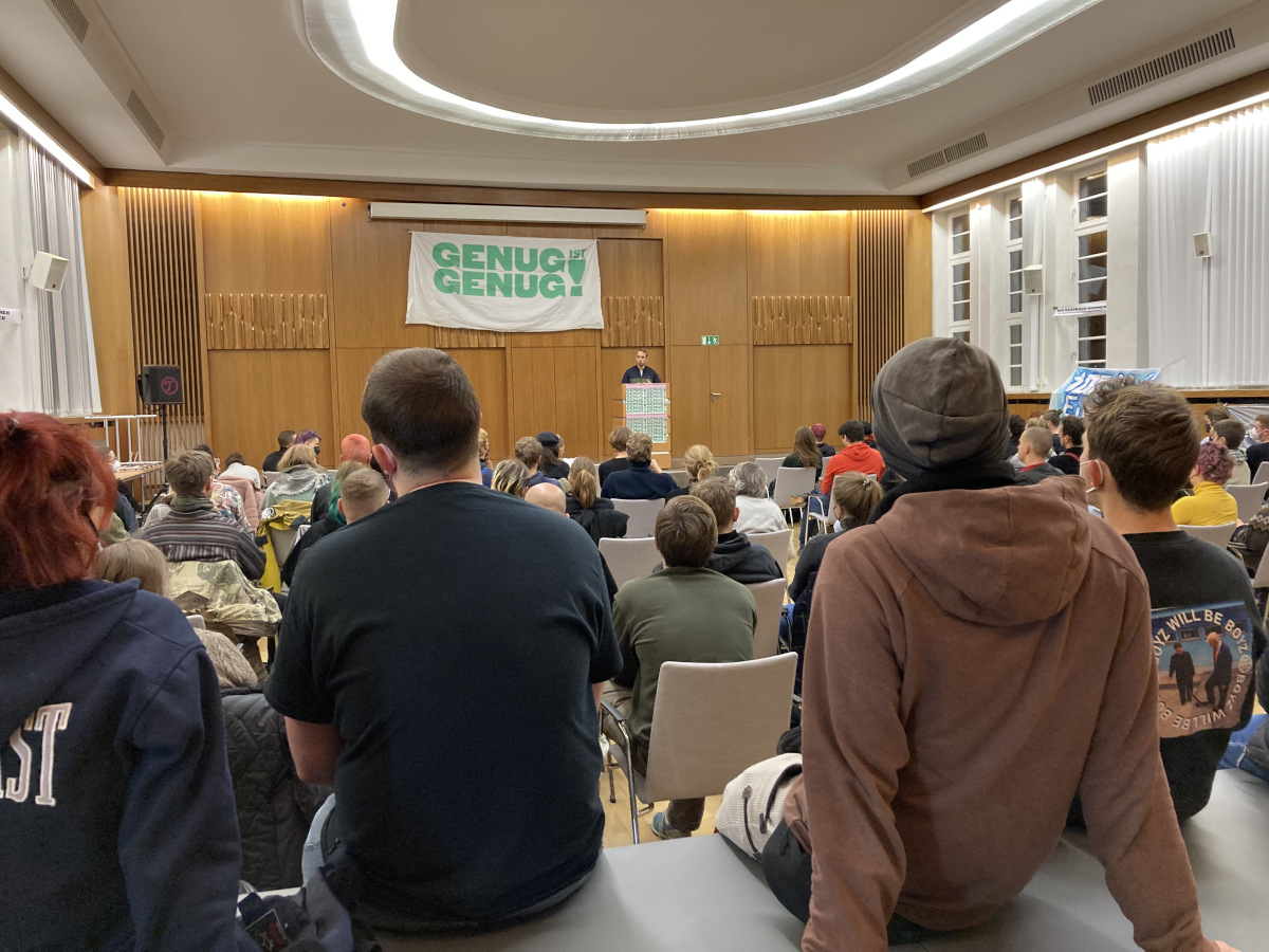 Blick auf eine Bühne, davor viele Menschen. Auf der Bühne ein Transparent mit der Aufschrift "Genug ist genug!"